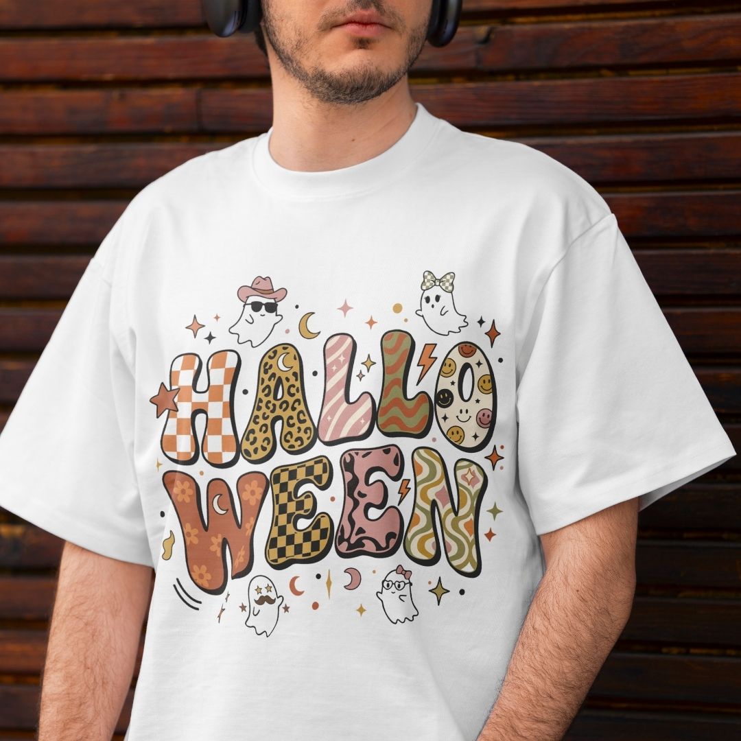 A man wearing a white graphic t-shirt with a colorful 'HALLOWEEN' text design featuring various animal print patterns, ghosts, and stars, set against a dark wooden background.