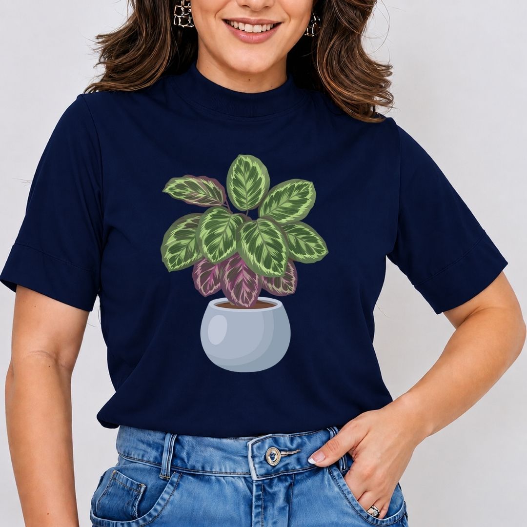 A woman wearing a navy blue short-sleeve t-shirt with a graphic of a potted green and purple calathea plant, paired with blue jeans against a light gray background.