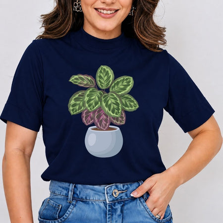 A woman wearing a navy blue short-sleeve t-shirt with a graphic of a potted green and purple calathea plant, paired with blue jeans against a light gray background.