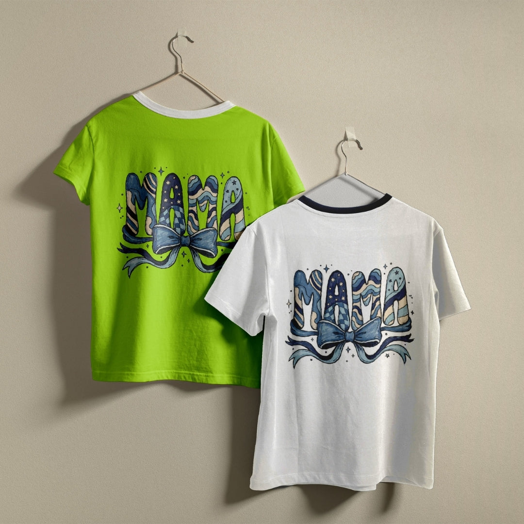 Two t-shirts hanging on a wall, one lime green and one white, both printed with a whimsical blue pattern "MAMA" coquette bow graphic.