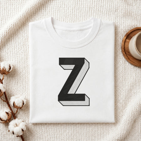 A folded white t-shirt with a large black block letter 'Z' printed on the front, styled on a textured cream fabric background with cotton bolls and a cup of coffee.