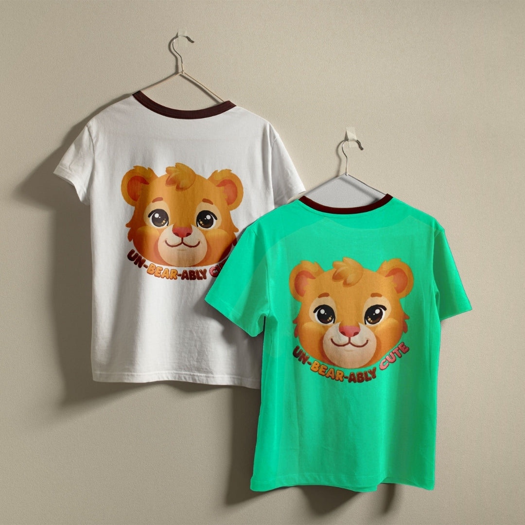 Two crewneck t-shirts, one white and one bright green, hanging against a wall displaying the cute bear Un-Bear-Ably Cute graphic print.