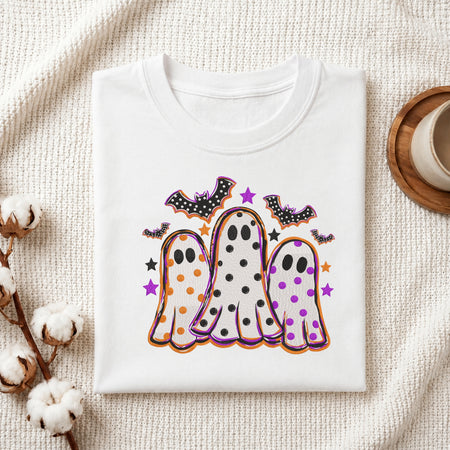 Folded white cotton t-shirt mockup featuring a cute Halloween ghosts and bats machine embroidery design, styled with cotton stems and a wooden cup
