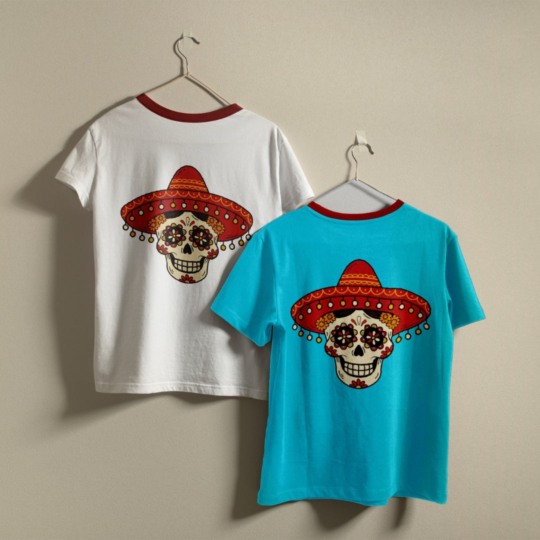 Two ringer t-shirts with red crew necks hanging on hangers against a beige wall. One shirt is white and the other is bright turquoise blue, both featuring a large sugar skull wearing a red sombrero graphic on the front.