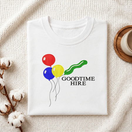  Folded white cotton t-shirt mockup featuring a colorful balloons and text machine embroidery design, styled with cotton stems and a wooden cup   