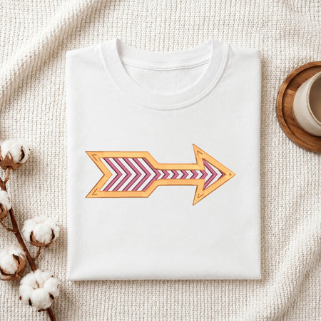 A folded white crewneck t-shirt with a graphic arrow design, styled on a textured cream fabric background with cotton bolls and a wooden cup.