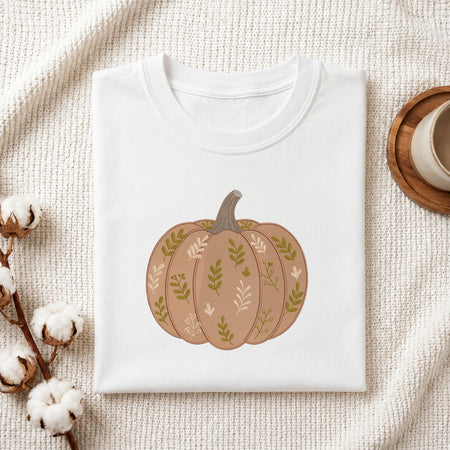  Folded white cotton t-shirt mockup featuring a leaf-patterned pumpkin machine embroidery design, styled with cotton stems and a wooden cup.   