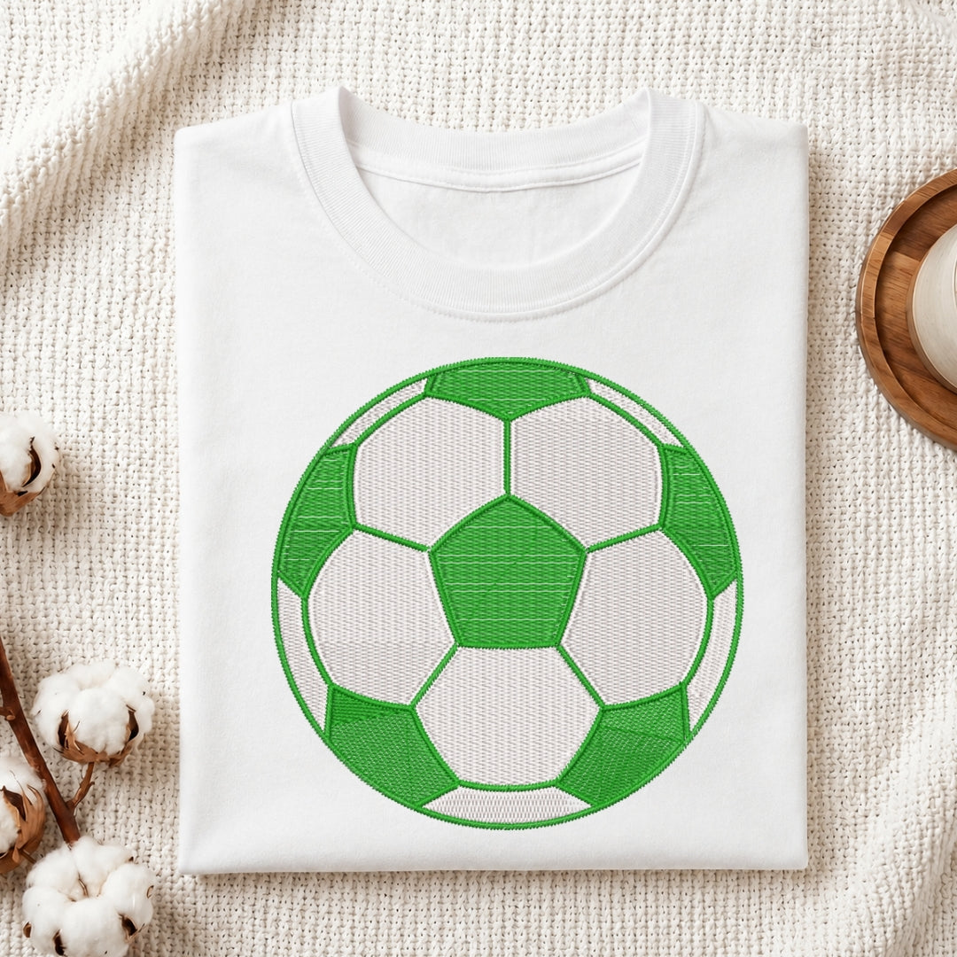 White t-shirt with a green soccer ball design on a textured surface.