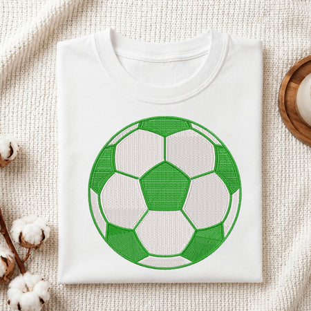 White t-shirt with a green soccer ball design on a textured surface.