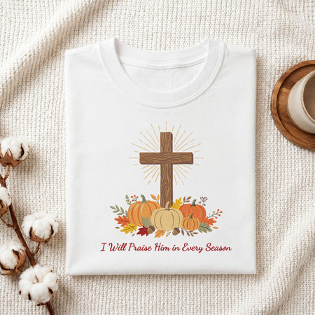 Folded white cotton t-shirt mockup featuring a Christian cross and autumn pumpkins machine embroidery design, styled with cotton stems and a wooden cup