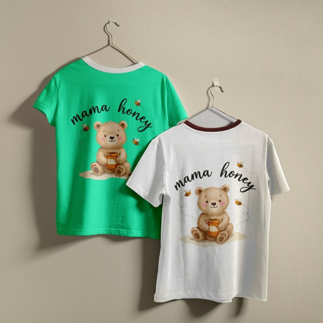 Two children's short-sleeve t-shirts hanging on hangers against a plain beige wall. The left shirt is bright green with a white collar and shows the back design featuring a teddy bear holding honey and the words 'mama honey' in black script.
