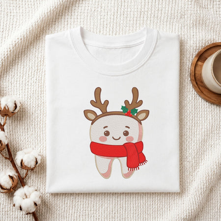  Folded white cotton t-shirt mockup featuring a cute smiling tooth wearing reindeer antlers and a red scarf Christmas dental machine embroidery design, styled with cotton stems and a wooden cup   