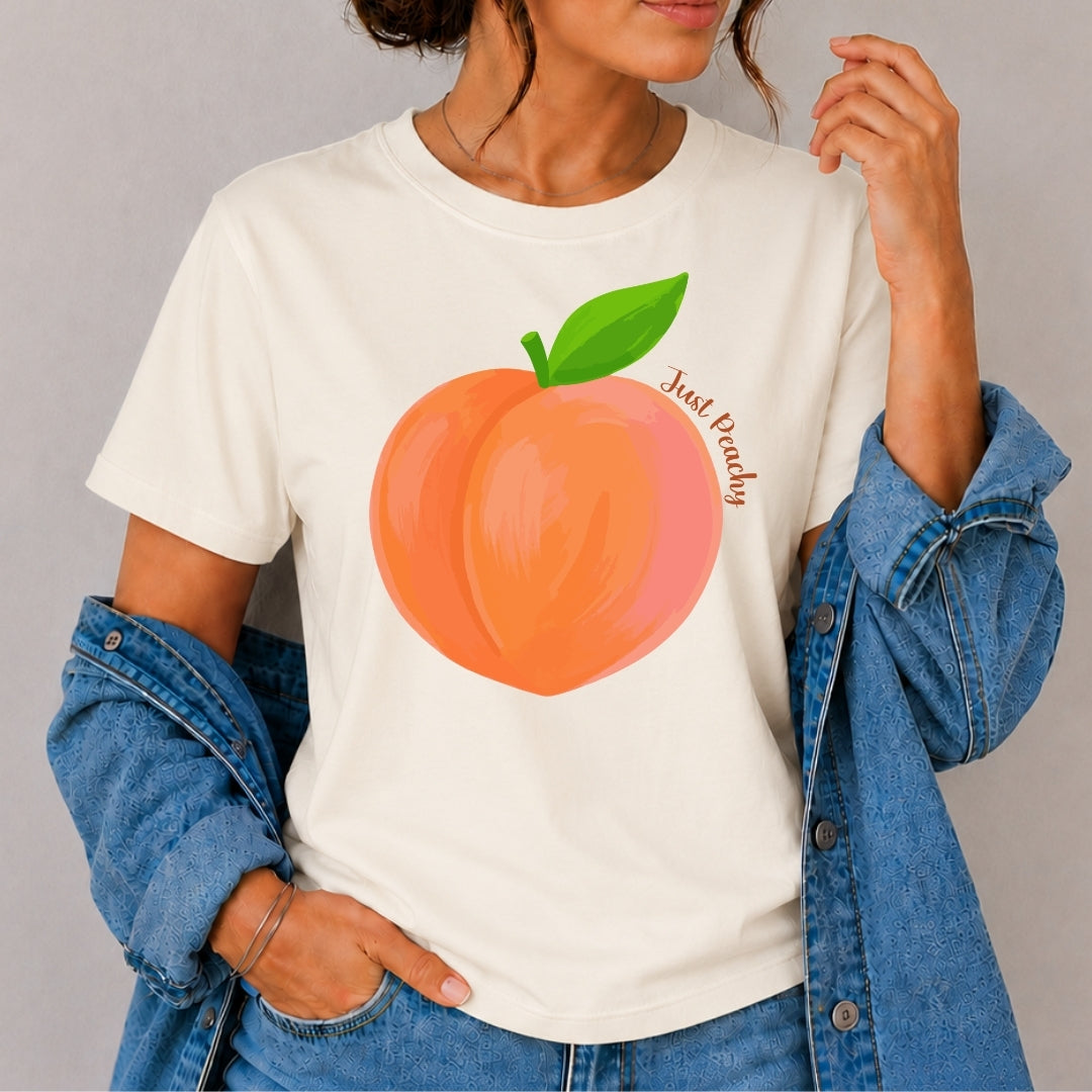 Person wearing a white t-shirt with a peach graphic and text, standing against a plain background.