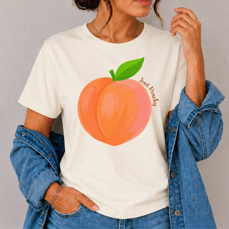 Person wearing a white t-shirt with a peach graphic and text, standing against a plain background.