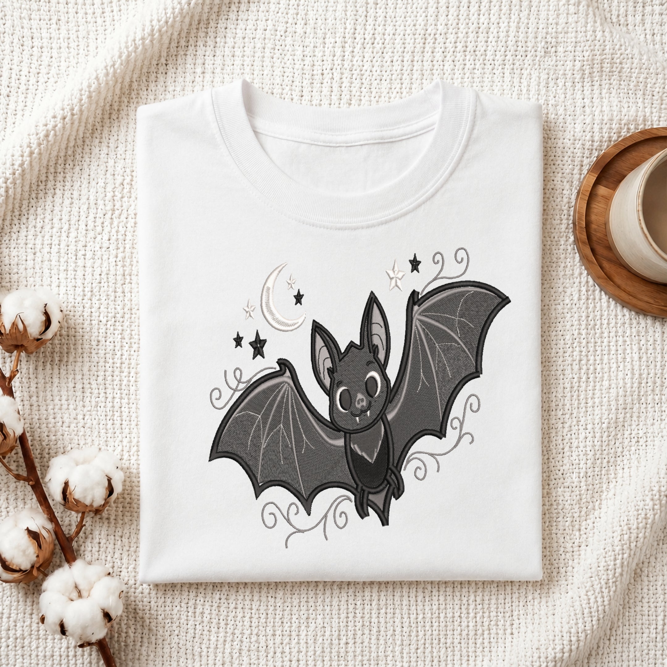 White folded t-shirt featuring a cute embroidered bat design.