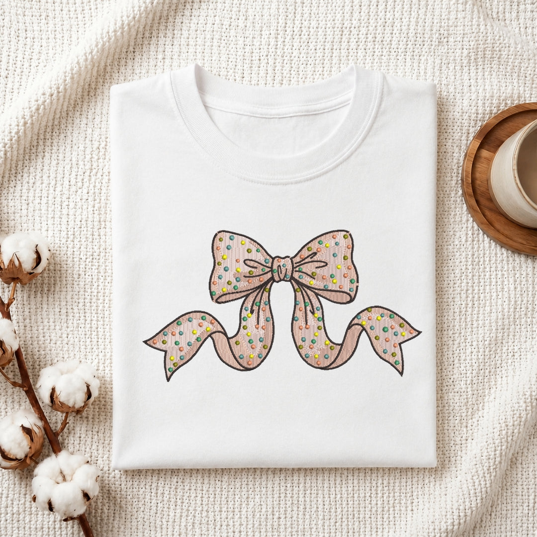 Polka dot bow embroidery stitched onto a folded white t-shirt.
