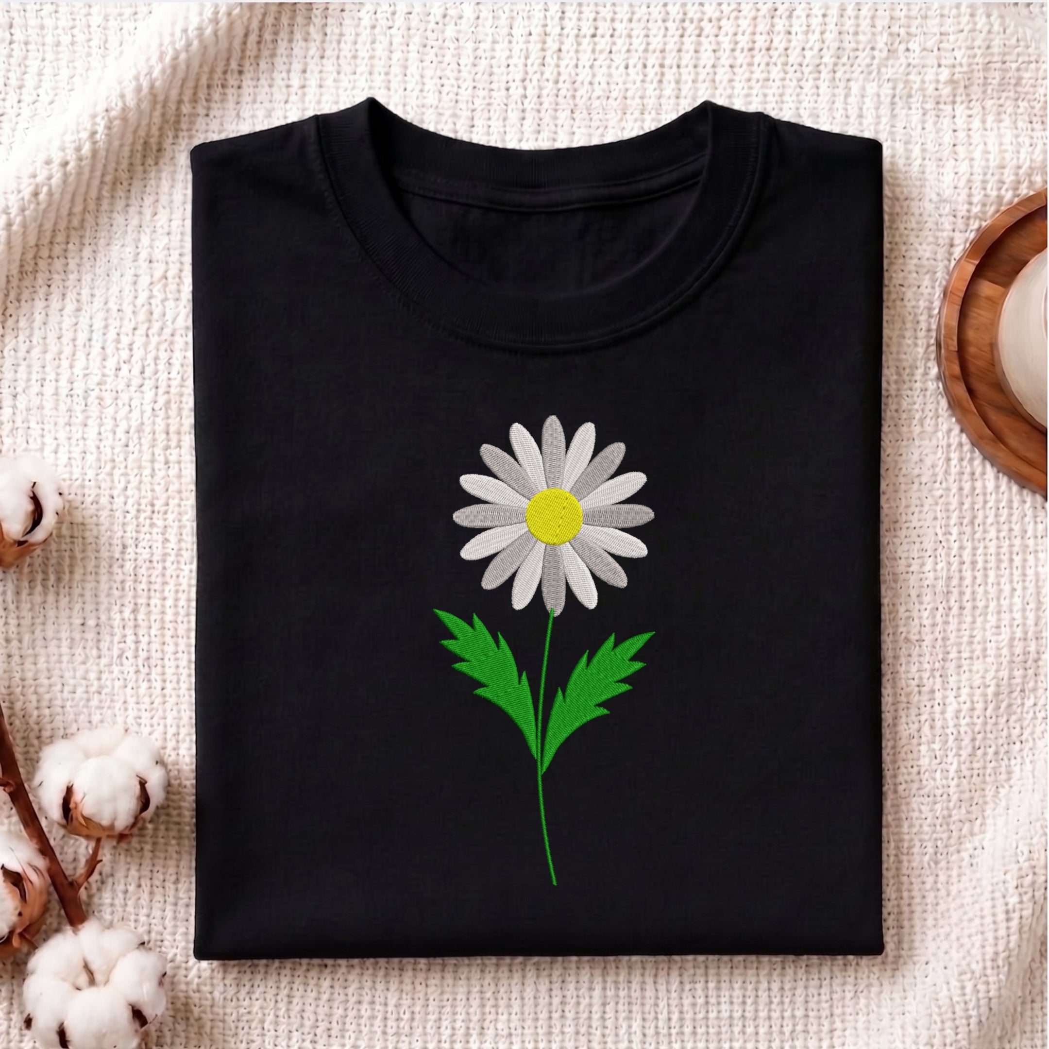 Folded black t-shirt featuring a white daisy flower embroidery design centered on the chest.