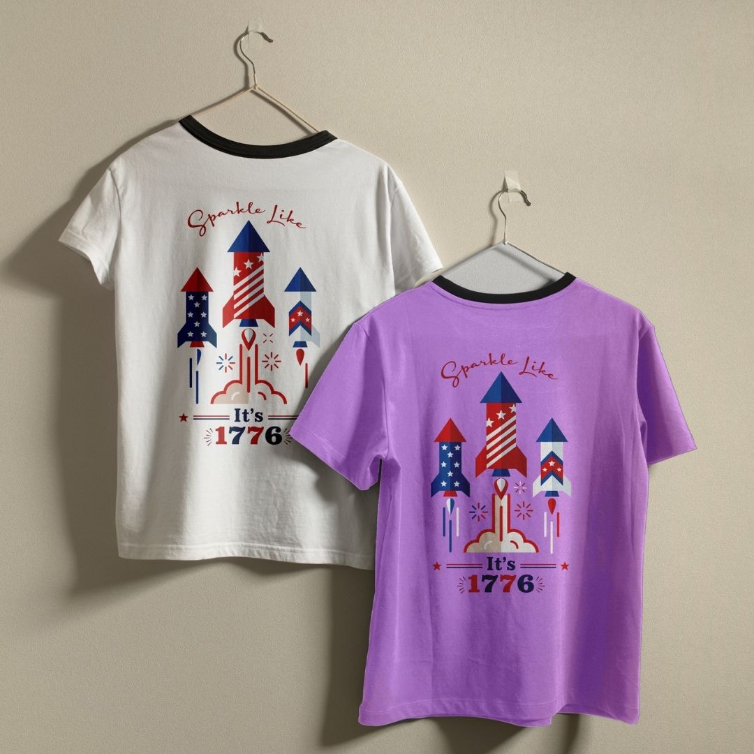 A white ringer t-shirt with a black collar and a solid purple t-shirt hanging on a wall, showcasing the "Sparkle Like It's 1776" custom design.
