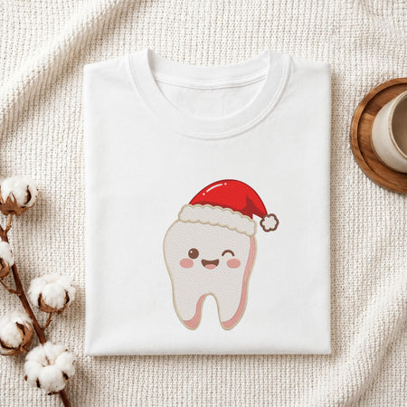 Folded white cotton t-shirt mockup featuring a cute winking tooth wearing a Santa hat Christmas dental machine embroidery design, styled with cotton stems and a wooden cup