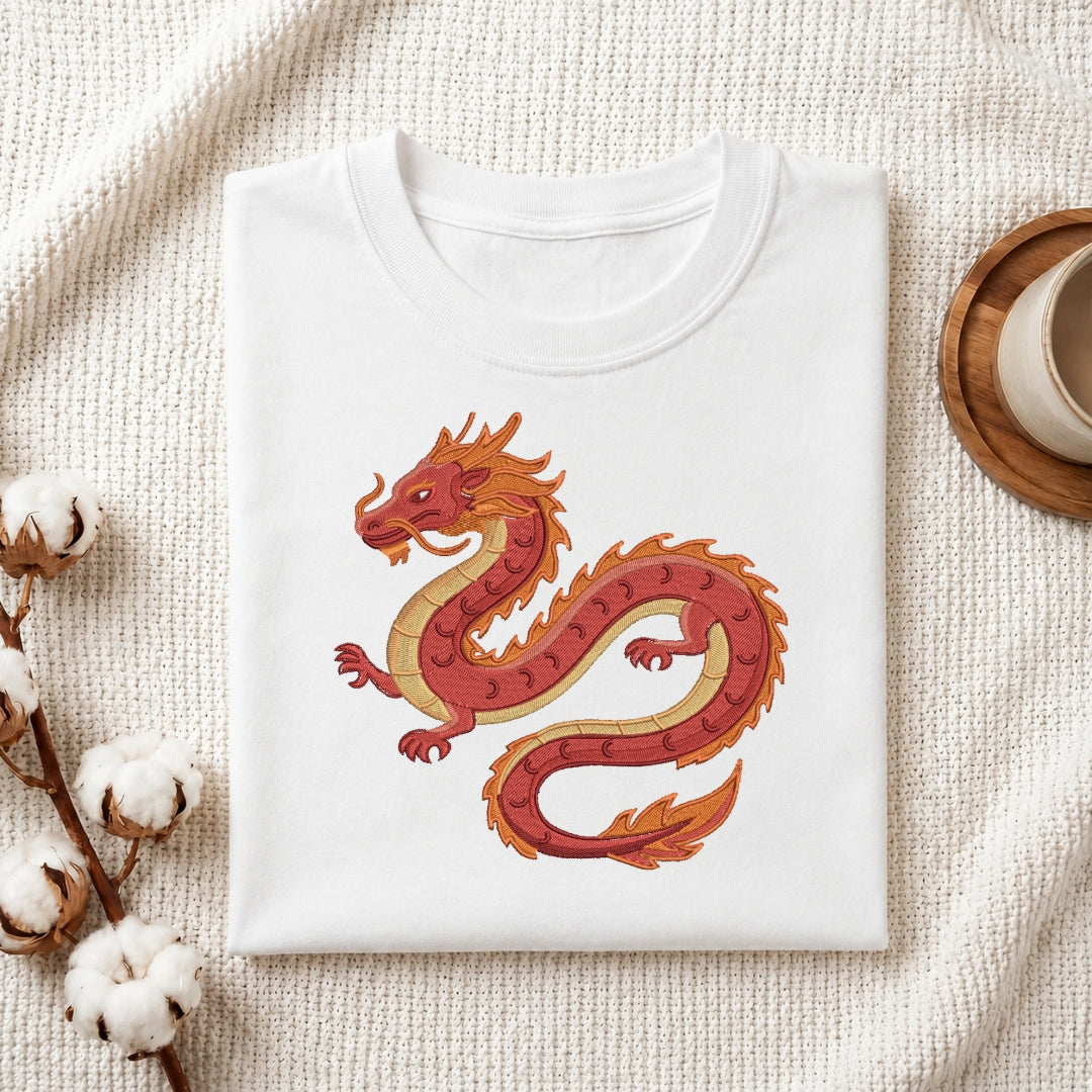A white t-shirt is folded neatly on a textured white surface, featuring an embroidered red and gold dragon design in the center.