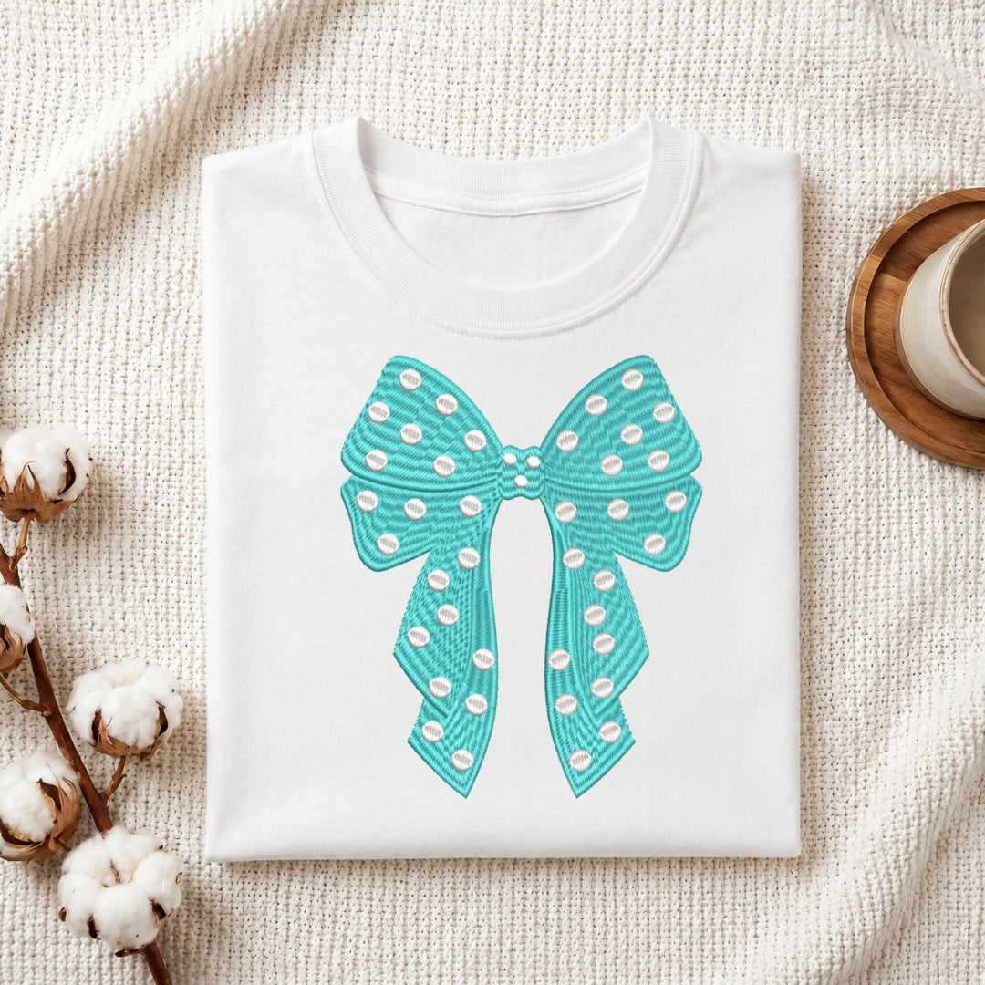 A white t-shirt featuring a teal embroidered bow design with white polka dots.