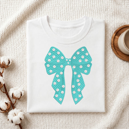 A white t-shirt featuring a teal embroidered bow design with white polka dots.