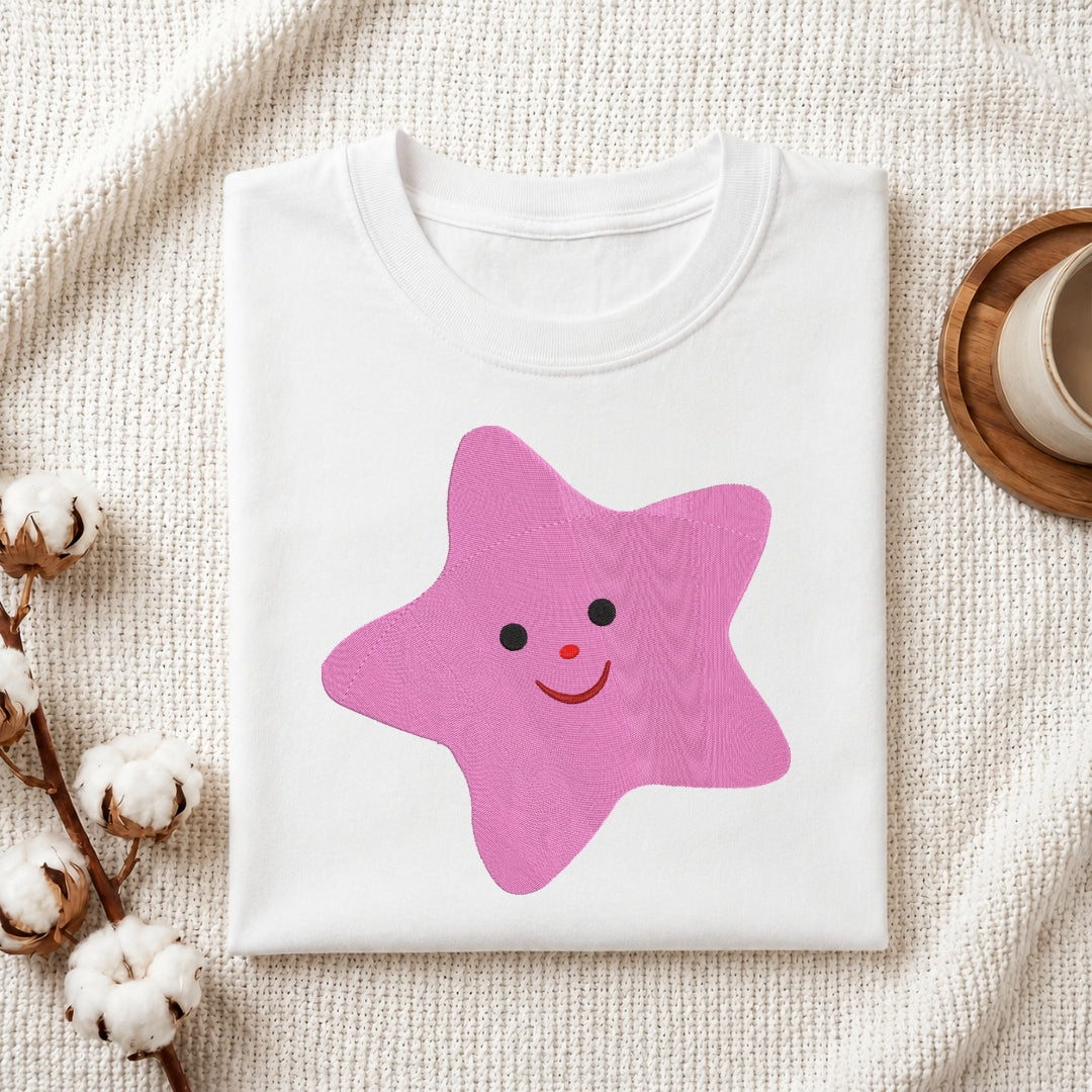 Adorable smiling pink star embroidery stitched onto a folded white t-shirt.