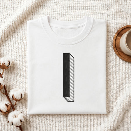 A folded white t-shirt with a minimalist black graphic of the number one, styled on a textured cream blanket with cotton bolls and a wooden cup in the background.