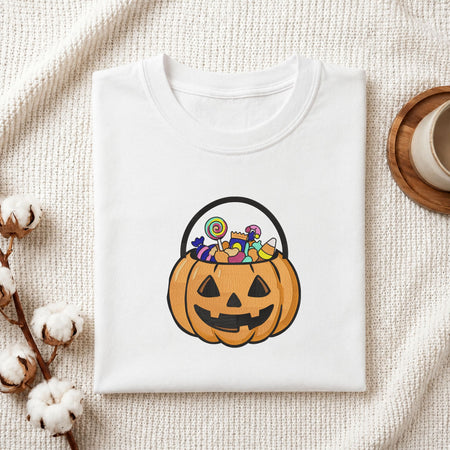  Folded white cotton t-shirt mockup featuring a jack-o'-lantern candy bucket machine embroidery design, styled with cotton stems and a wooden cup   