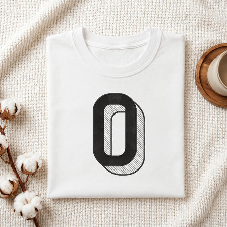 A neatly folded white crewneck t-shirt featuring a stitched 3D block letter "O" design, styled with cotton branches and a wooden coaster.