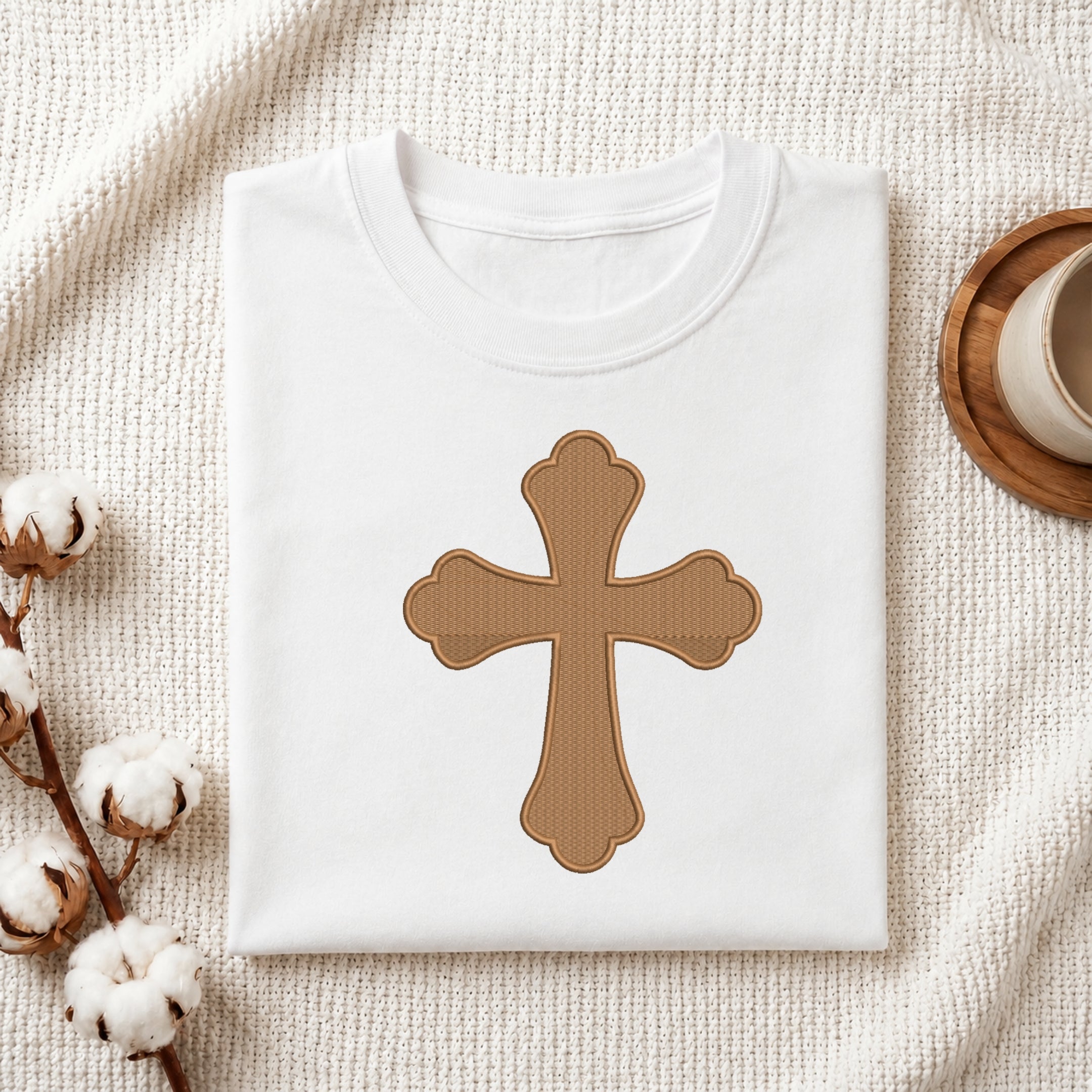 Folded white cotton t-shirt featuring a brown scalloped cross embroidery design centered on the chest.