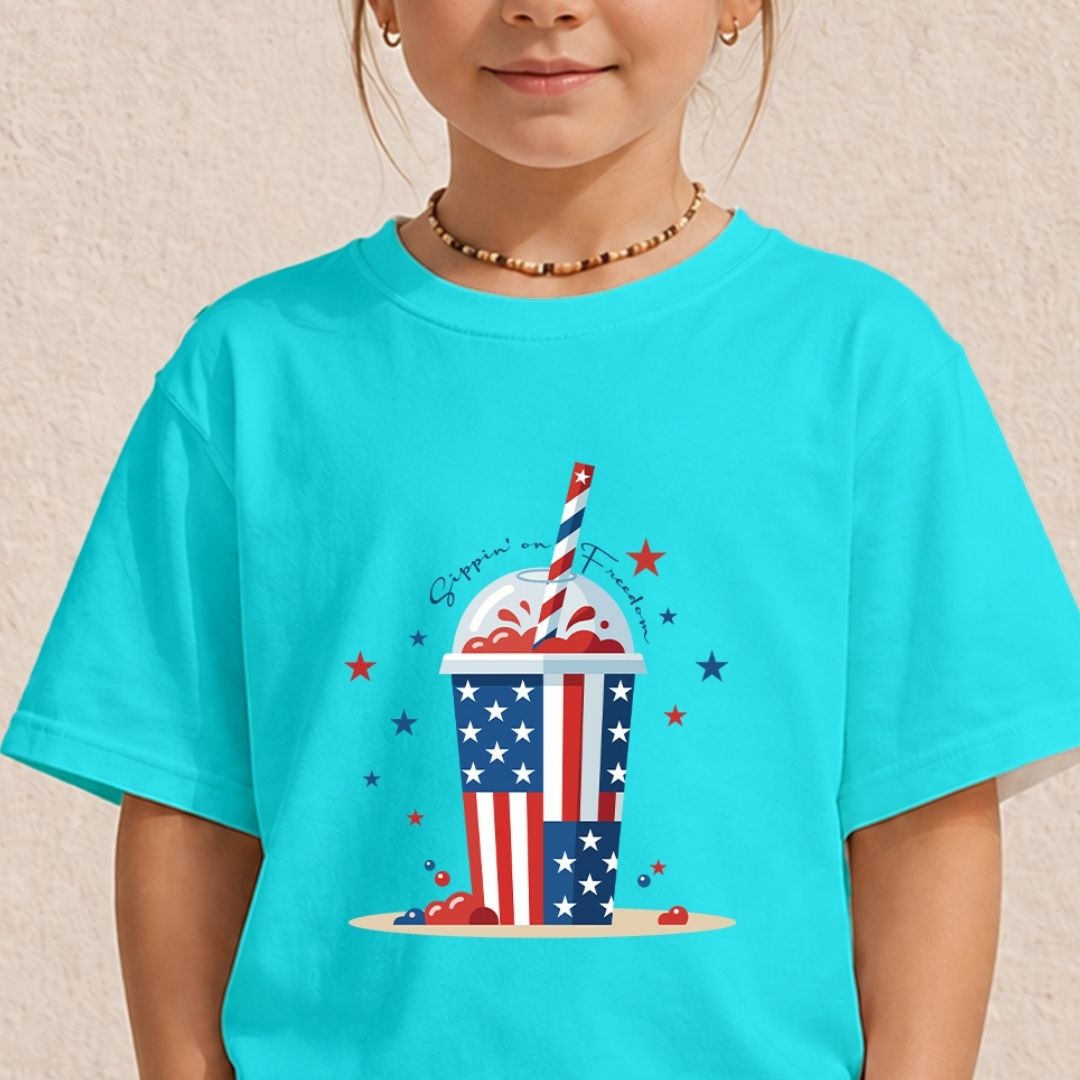 A young child wearing a bright cyan turquoise t-shirt displaying a colorful "Sippin' on Freedom" frozen drink graphic on the front.