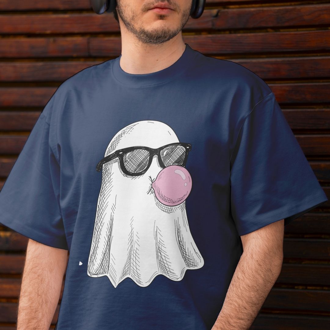 A man wearing a navy blue t-shirt with a graphic of a white ghost wearing black sunglasses and blowing a pink bubblegum bubble, set against a dark wooden plank background.