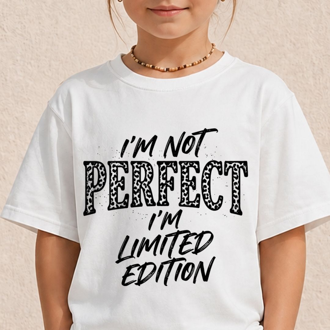 A child wearing a white short-sleeve graphic T-shirt with the text 'I'M NOT PERFECT I'M LIMITED EDITION' in black lettering, photographed against a light beige textured wall.