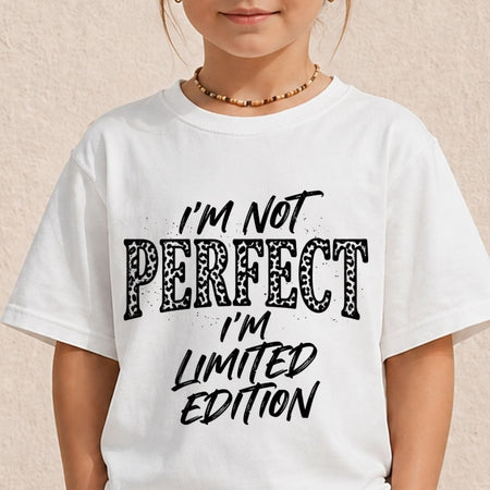 A child wearing a white short-sleeve graphic T-shirt with the text 'I'M NOT PERFECT I'M LIMITED EDITION' in black lettering, photographed against a light beige textured wall.