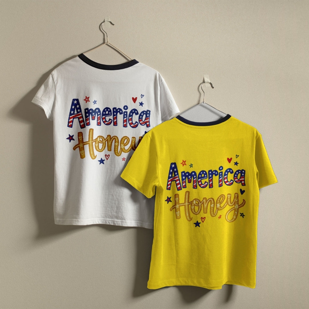 Two kids' ringer t-shirts hanging on hangers against a plain beige wall. One shirt is white with a navy collar, and the other is bright yellow with a navy collar.