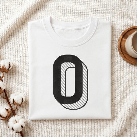 A folded white crewneck t-shirt with a large black graphic letter 'O' on the front, styled on a textured cream blanket with cotton bolls and a wooden cup in the background.