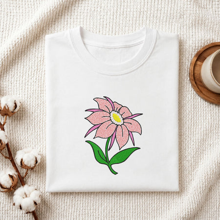 Folded white cotton t-shirt mockup featuring a pink flower machine embroidery design, styled with cotton stems and a wooden cup