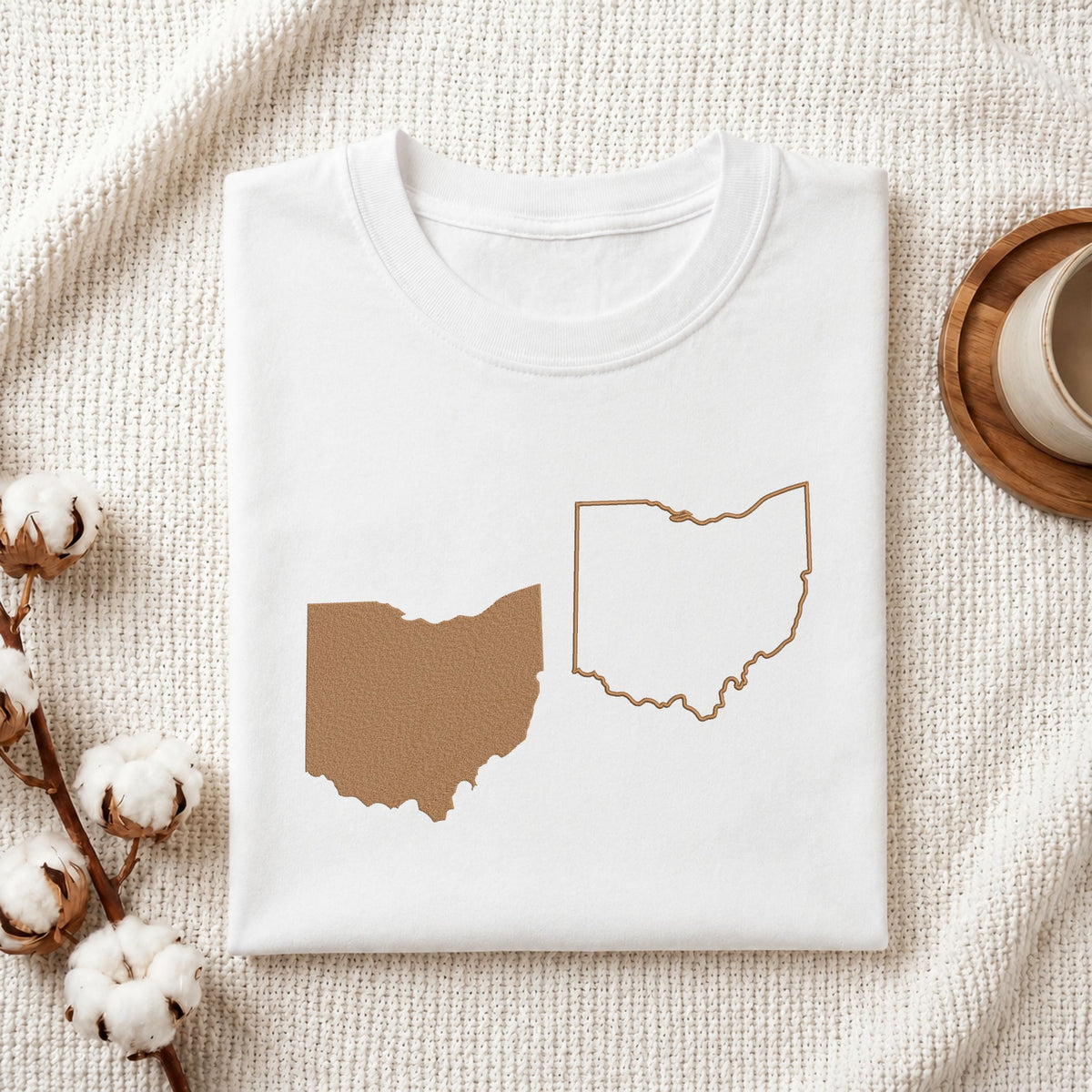 Folded white cotton t-shirt mockup featuring Ohio state map machine embroidery designs, styled with cotton stems and a wooden cup.