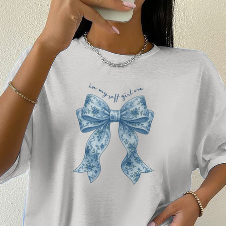 White t-shirt with blue floral bow graphic and text 'in my soft girl era' worn by a person.