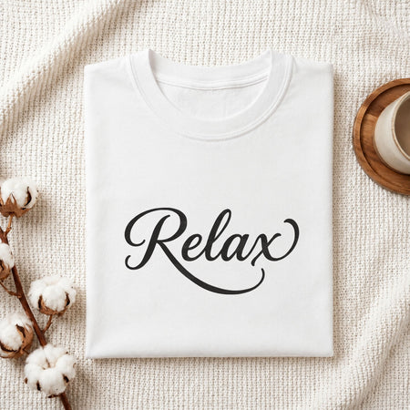 Folded white cotton t-shirt mockup featuring a "Relax" script machine embroidery design, styled with cotton stems and a wooden cup   