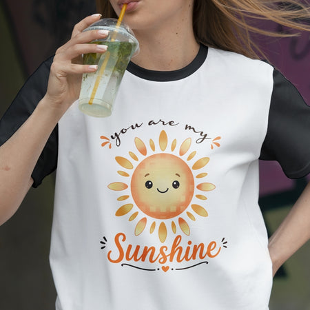 Person wearing a t-shirt with a sun graphic and 'you are my sunshine' text, holding a drink.