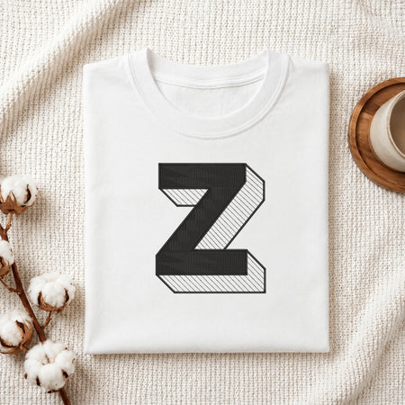 A folded white t-shirt with a large black 3D-style letter 'Z' printed on the front, styled on a textured cream fabric background with cotton bolls and a cup of coffee.