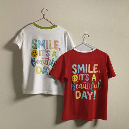 Two children's short-sleeve t-shirts hanging on hangers against a plain beige wall. The front shirt is bright red with a white collar and colorful text reading 'SMILE, IT'S A Beautiful DAY!' with a yellow smiley face.