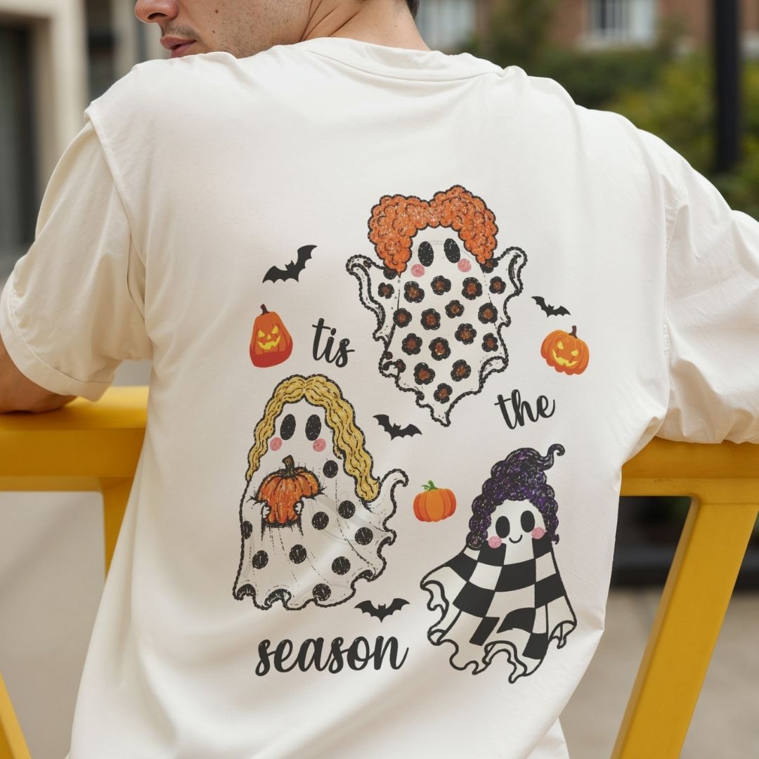 A person wearing a white short-sleeve T-shirt, shown from the back, with a large Halloween-themed graphic print featuring three ghost characters, pumpkins, bats, and the words 'tis the season'.