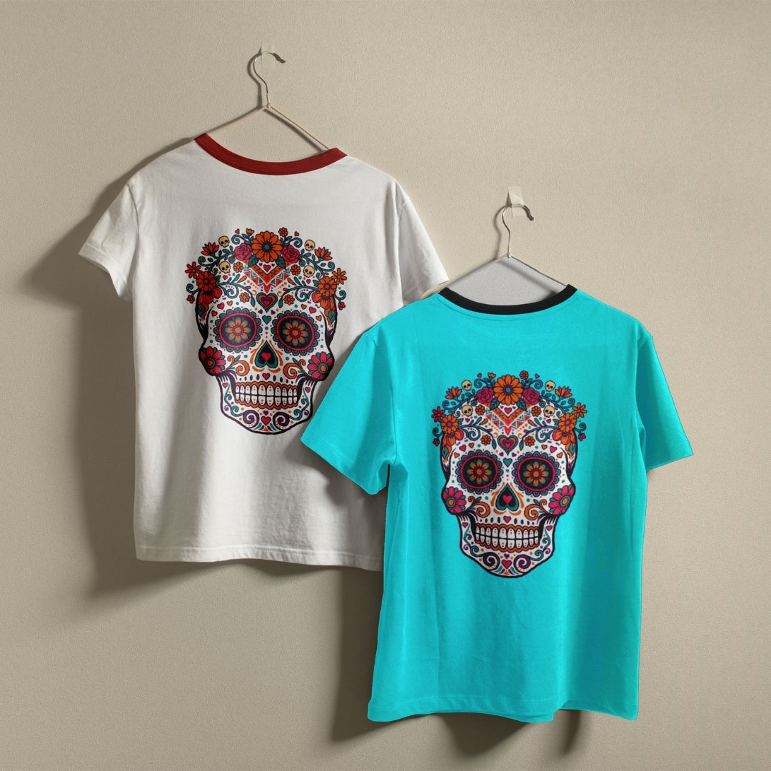 Two ringer t-shirts with colorful sugar skull prints hanging on hangers against a beige wall. One shirt is white with a red collar, showing the back design.