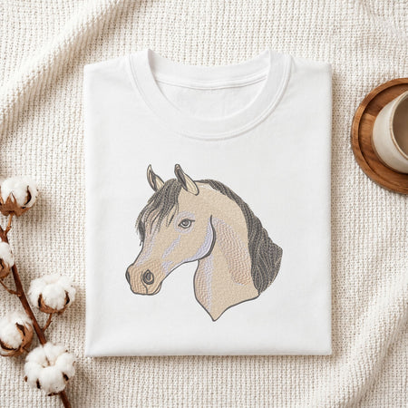 Folded white cotton t-shirt mockup featuring an elegant horse head machine embroidery design, styled with cotton stems and a wooden cup   