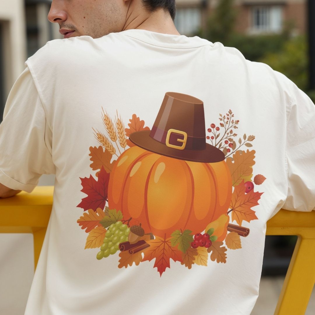 A man wearing a white t-shirt from behind, showing a large autumn-themed graphic print of a pumpkin wearing a brown Pilgrim hat surrounded by colorful fall leaves, berries, and wheat.
