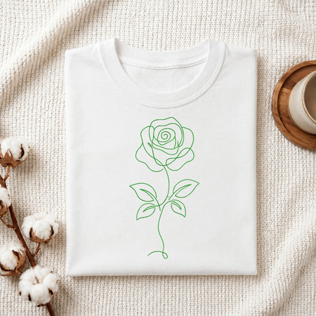 A green minimalist single line art rose embroidery design stitched on the front of a folded white cotton t-shirt.