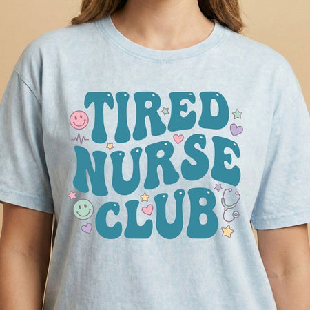 Light blue t-shirt with 'TIRED NURSE CLUB' text and graphics on a beige background